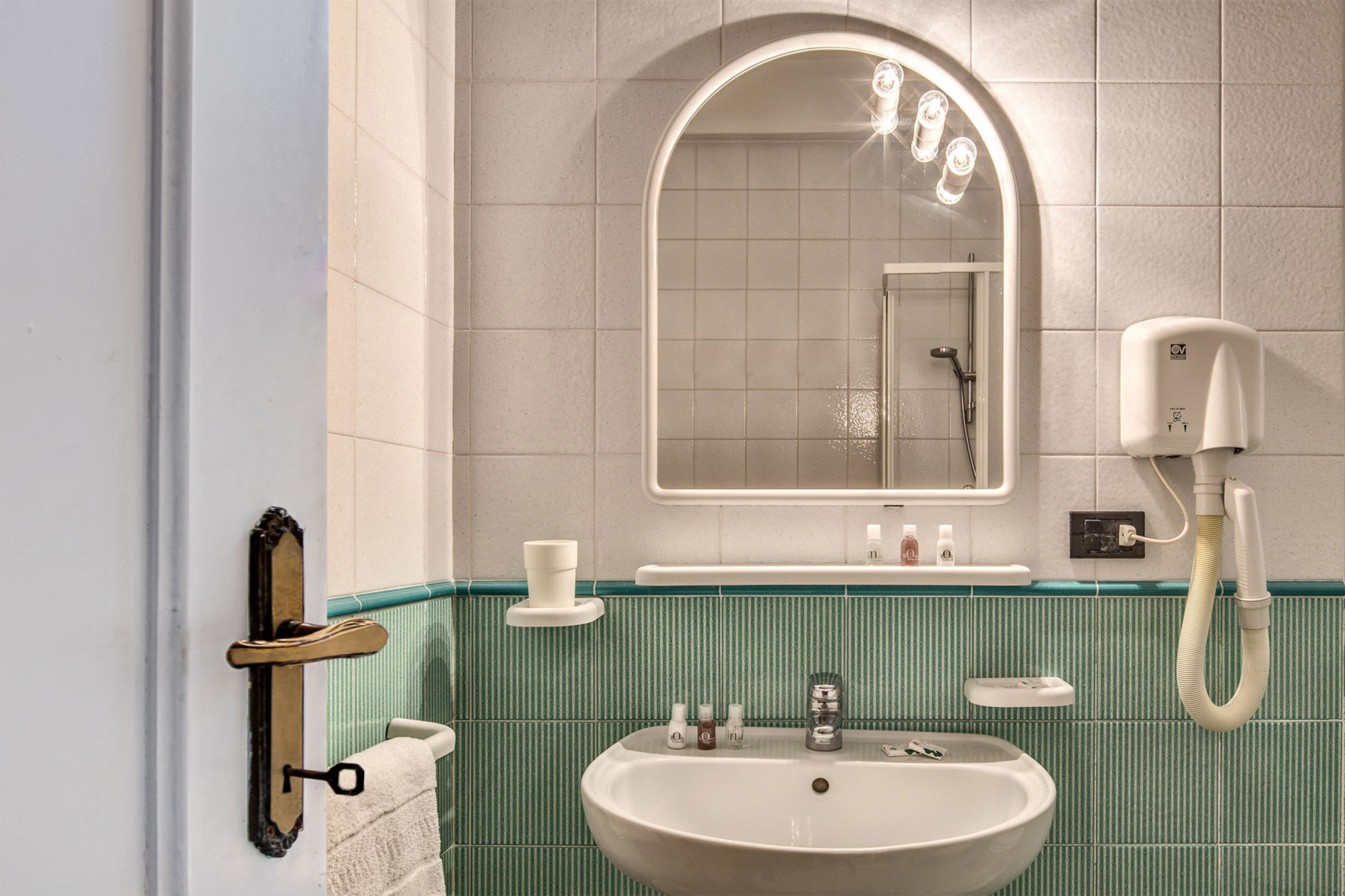 Un baño con un lavamanos blanco, un espejo y un cabezal de ducha de mano.