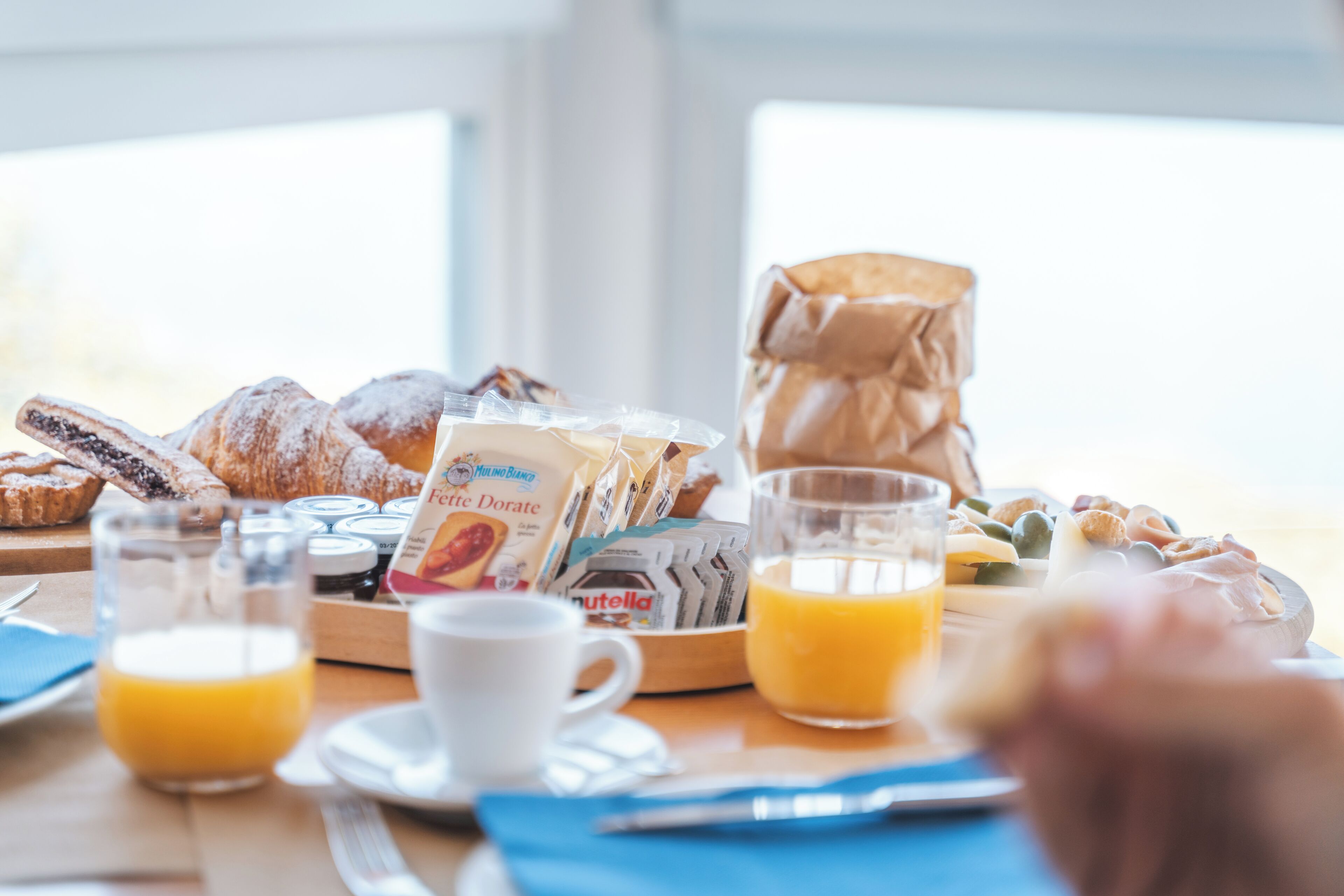 A breakfast table with pastries, Nutella, juice, and a coffee cup.