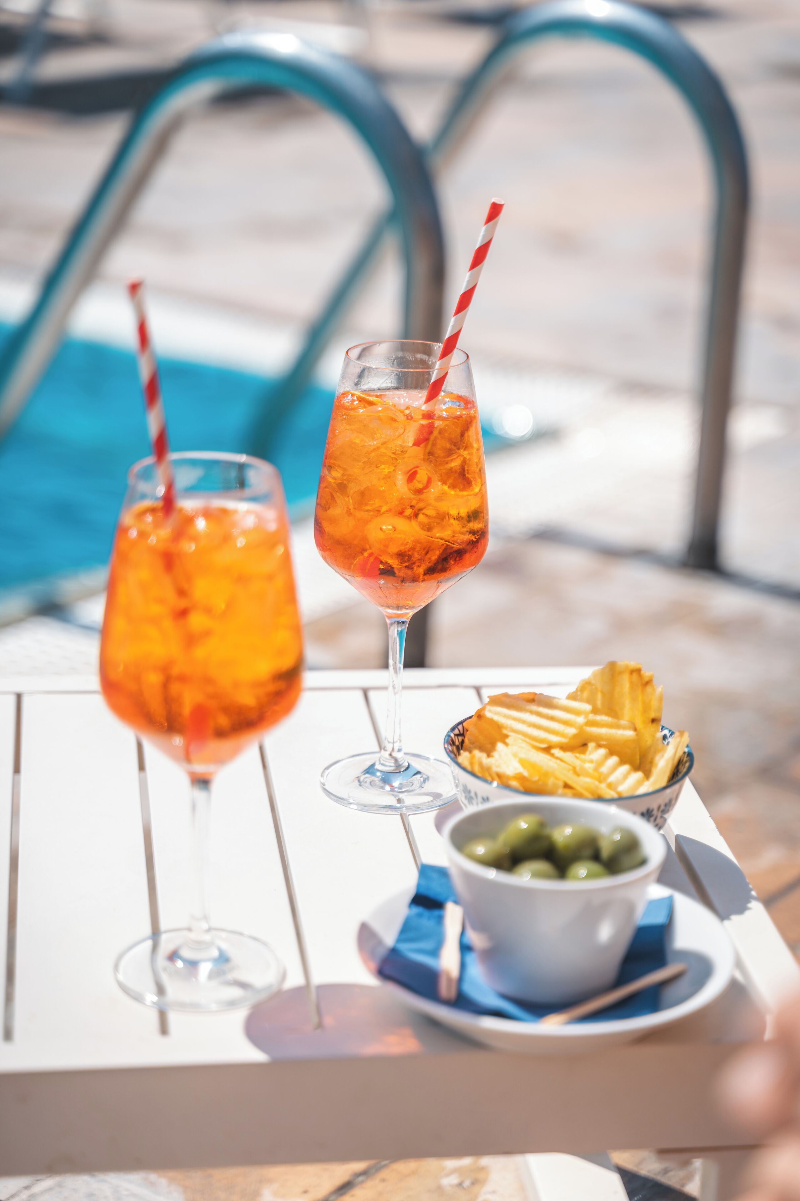 A table with two drinks, a bowl of chips, and a bowl of olives.