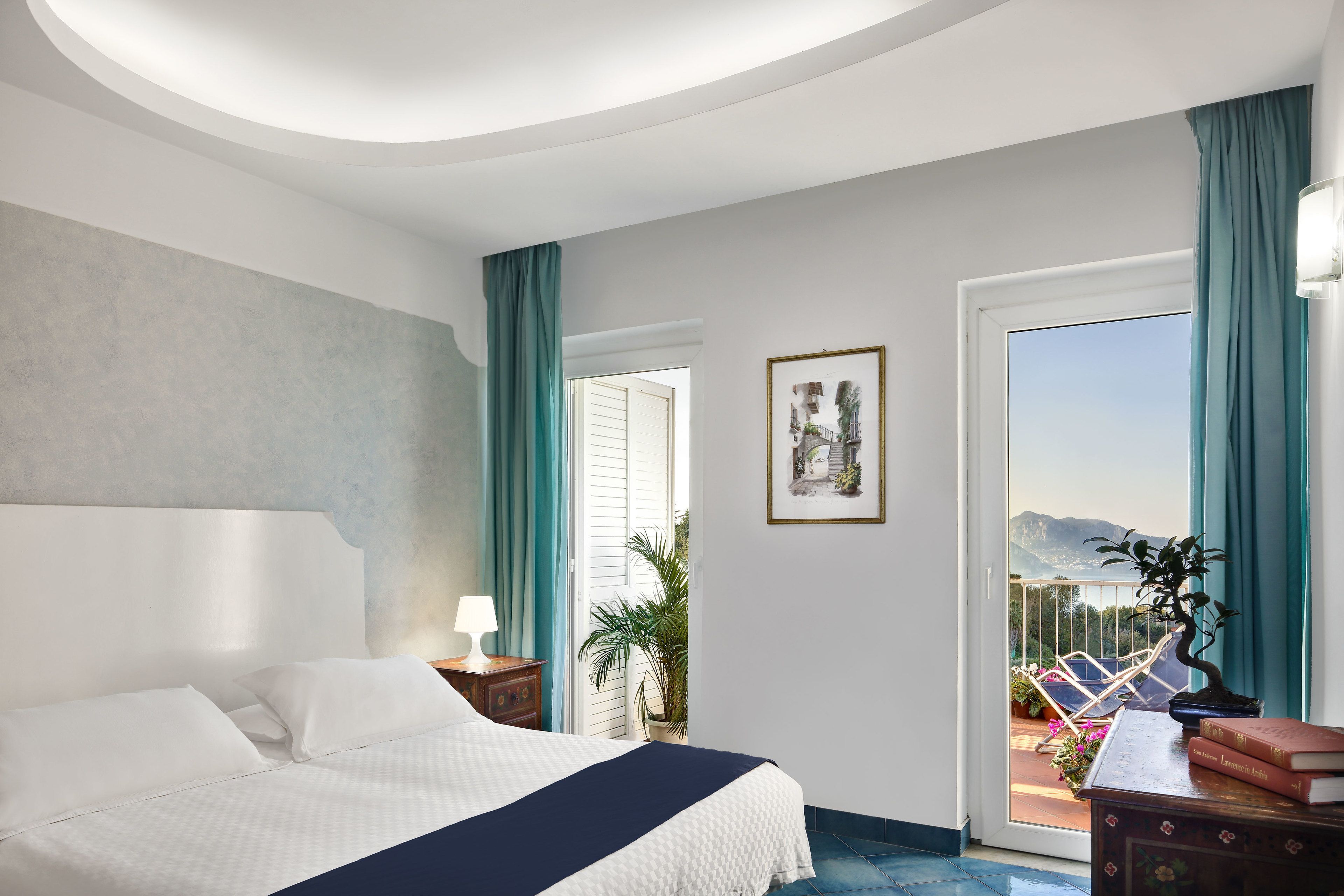 Habitación de hotel con cama, mesita de noche, lámpara, planta en maceta, cuadro enmarco y vistas al exterior.