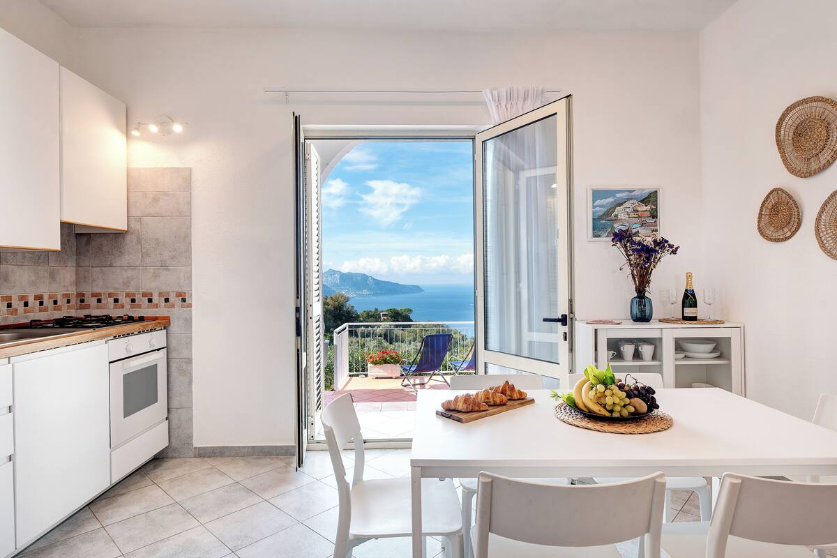 Eine moderne Küche mit Meerblick, ein Essbereich mit Tisch für zwei Personen und ein Balkon mit Stuhl.