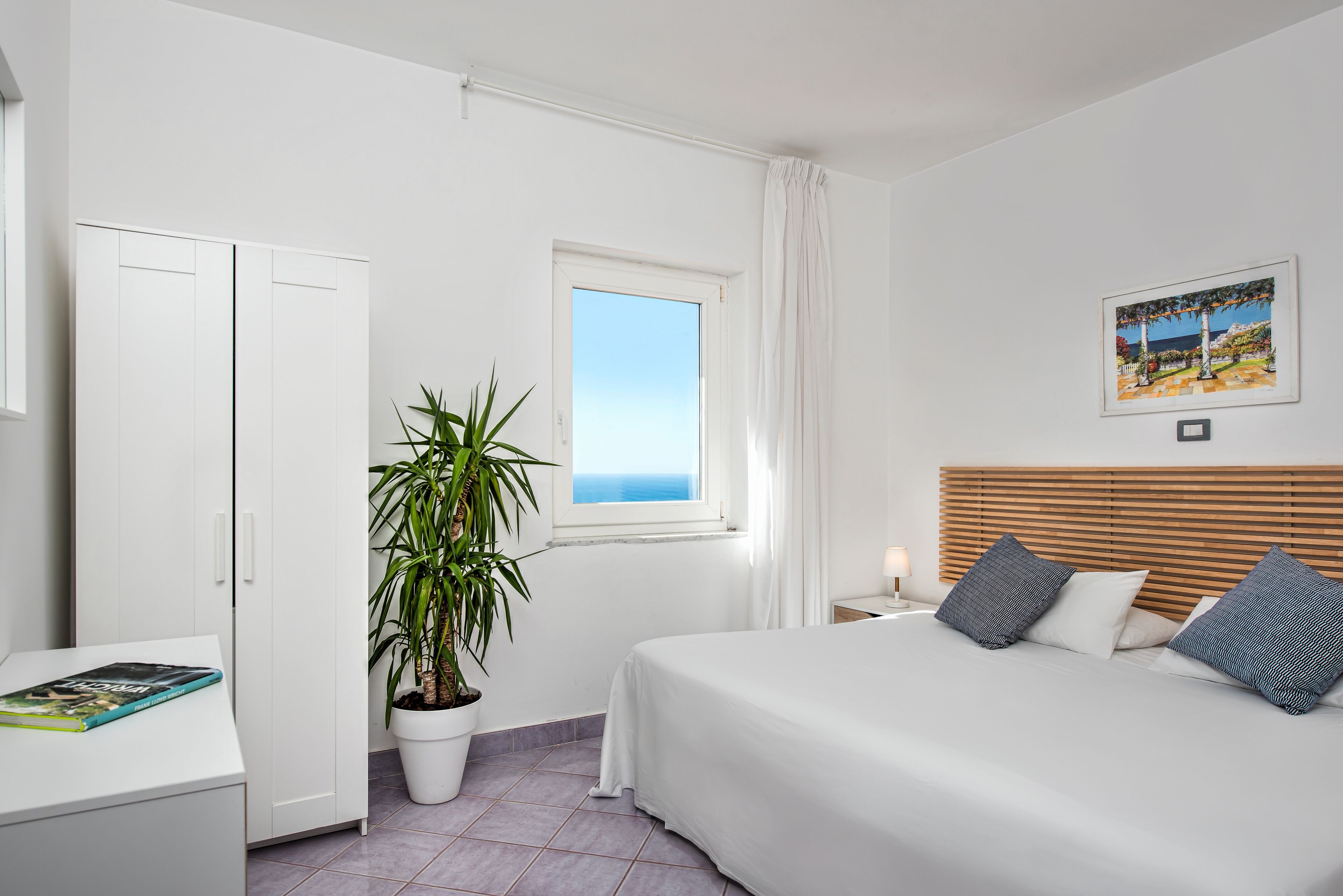 Une chambre à coucher avec un lit, une table de chevet, une plante en pot, une fenêtre et une porte.