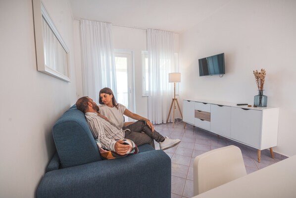 Una sala de estar con un sofá, un televisor montado en la pared, una lámpara y un mueble.