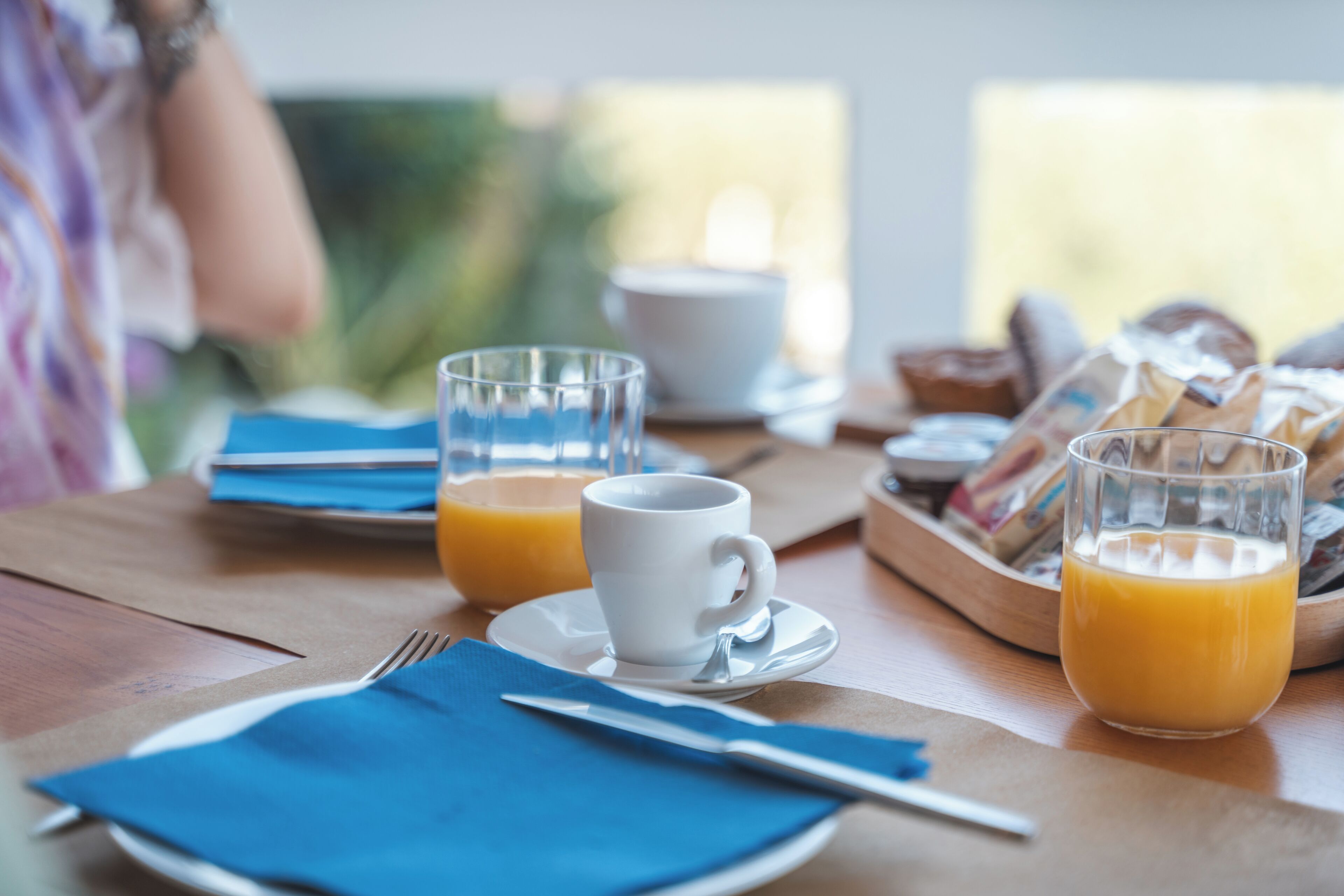 Une table mise pour le petit-déjeuner, avec une table, des assiettes, des tasses et un panier de pain.
