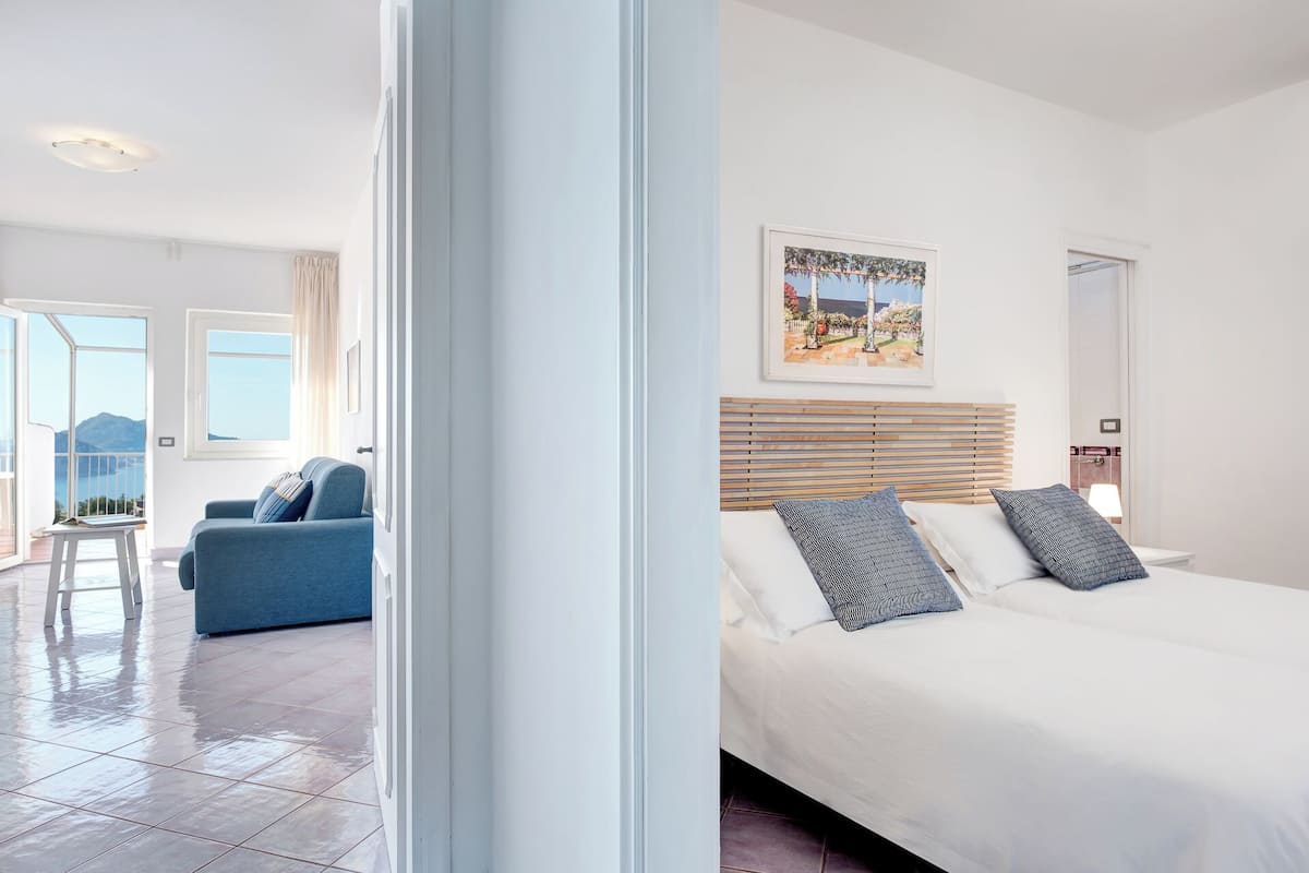 Ein modernes Schlafzimmer mit einem großen Bett, Blick ins Freie und einem Balkon mit einem Stuhl.