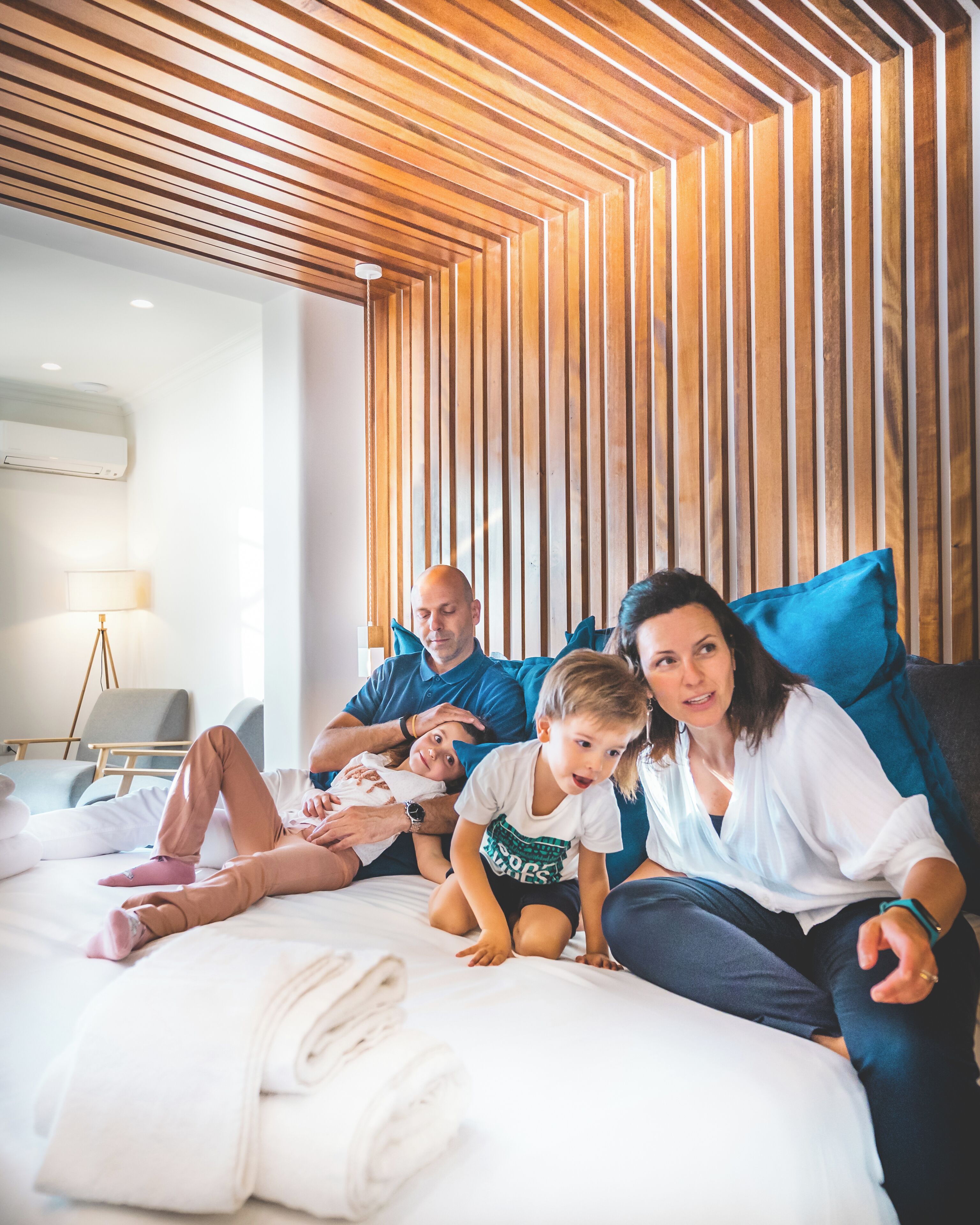A family on a bed in a hotel room with a wooden slatted ceiling and a modern design.