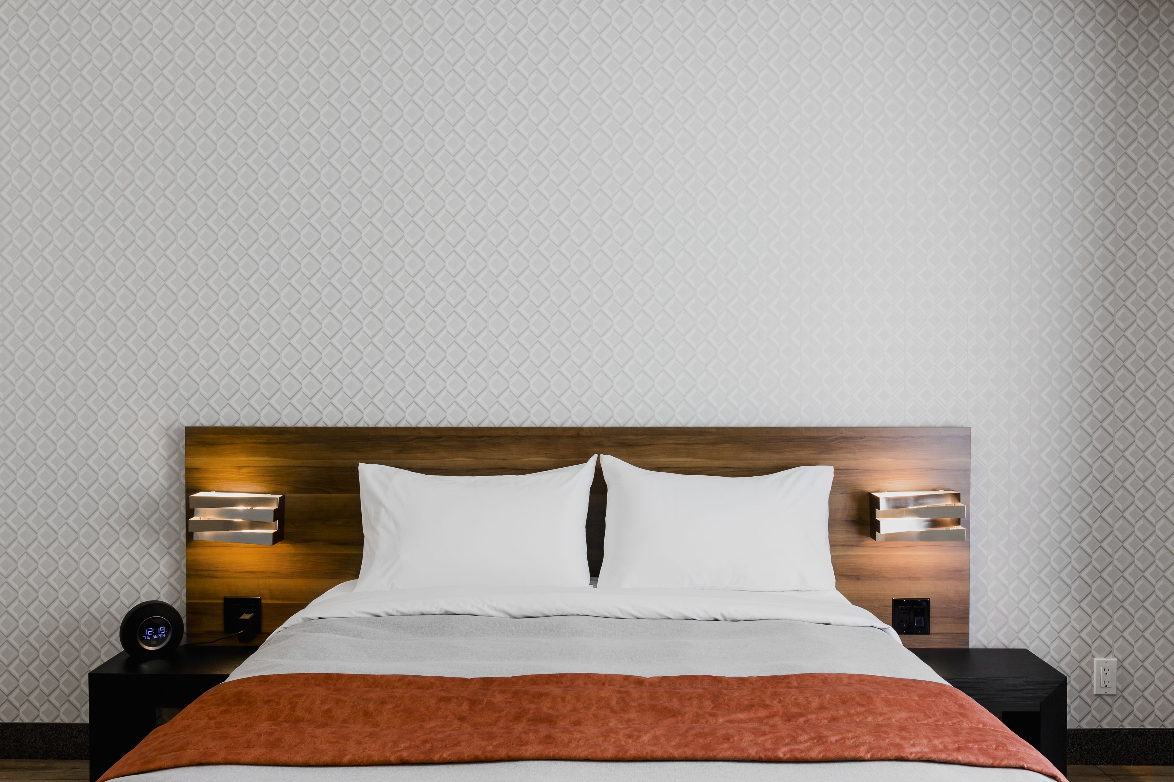 A neatly made bed with a wooden headboard, white pillows, and a brown throw blanket.