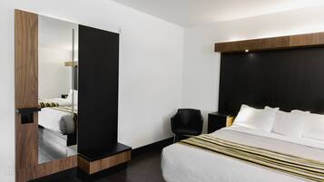 Una habitación de hotel moderna con una cama grande, una silla negra, una mesita de noche y un espejo.
