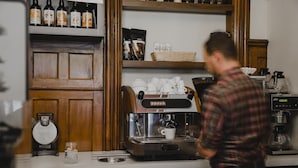 Interior de una cafetería con una máquina de café, tazas y estantes con botellas de café.