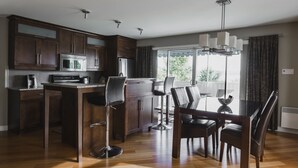 Una cocina moderna con armarios de madera oscura, un microondas de acero inoxidable y una zona de comedor con una mesa de vidrio y cuatro sillas.