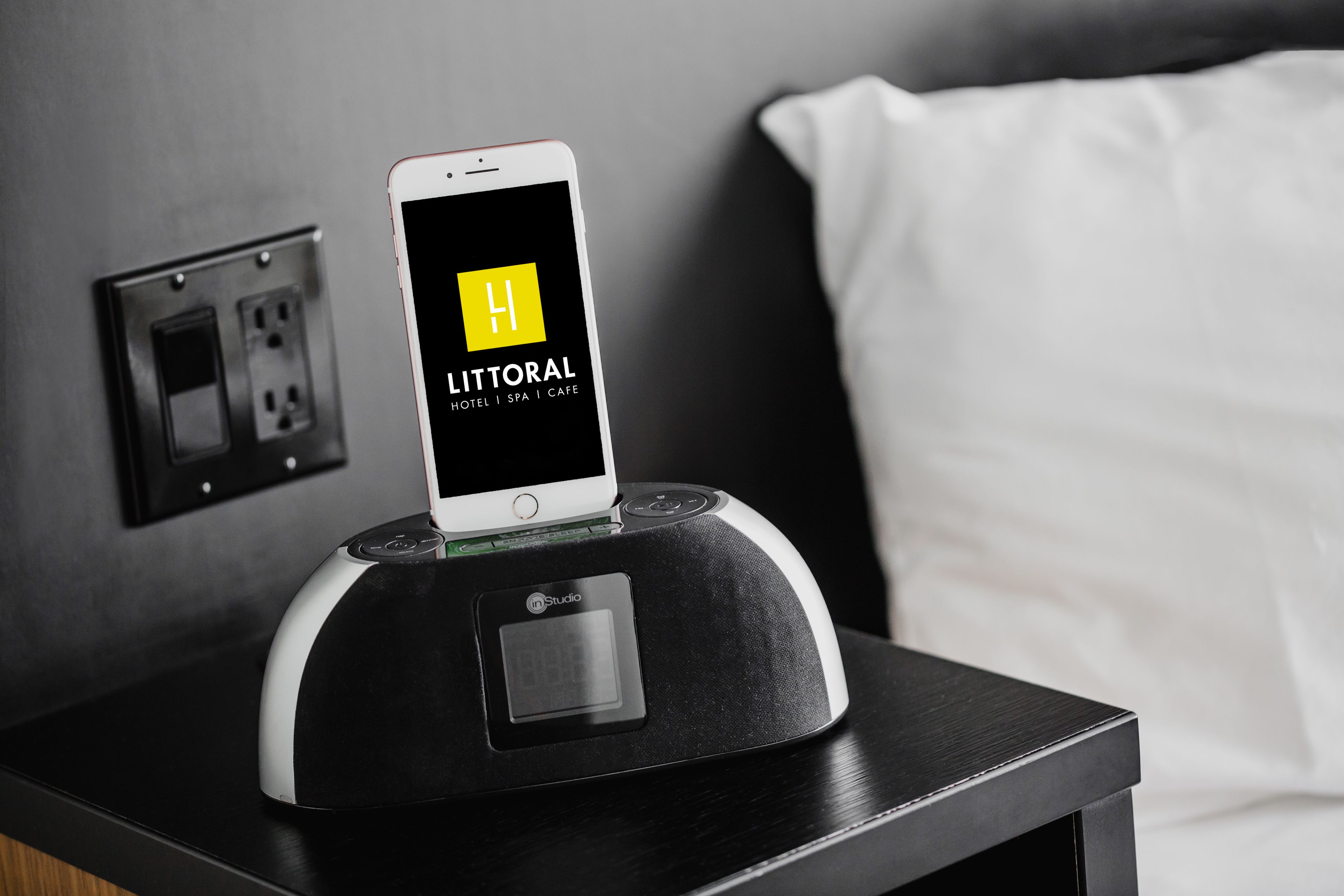 Un teléfono inteligente en una base de carga, mostrando en su pantalla la aplicación de un hotel con la leyenda 'LITTORAL HOTEL | SPA | CAFE'.