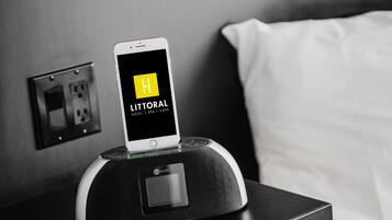 Un teléfono inteligente en una base de carga, mostrando en su pantalla la aplicación de un hotel con la leyenda 'LITTORAL HOTEL | SPA | CAFE'.