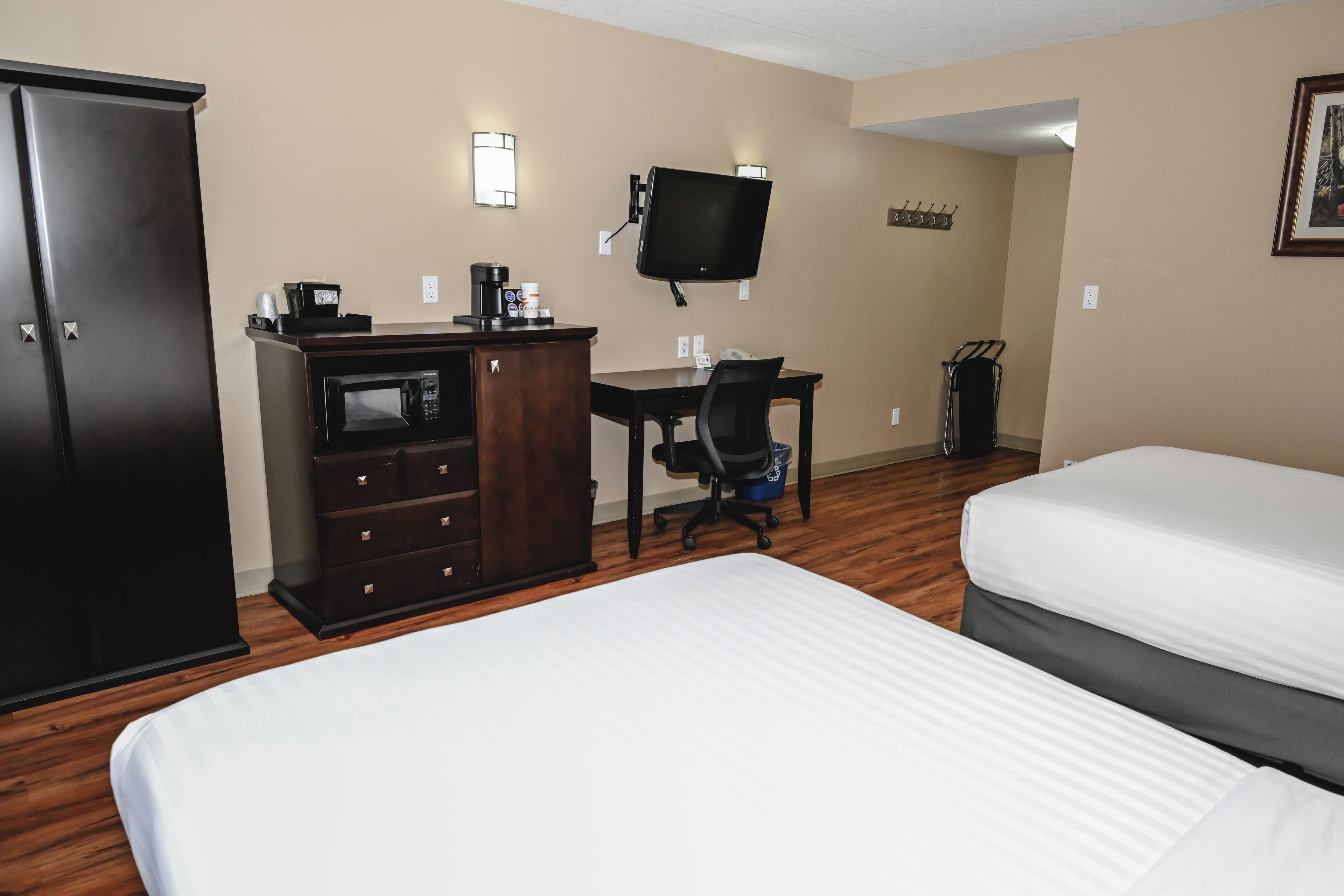 A hotel room with two beds, a desk with a computer, a television, and a wardrobe.
