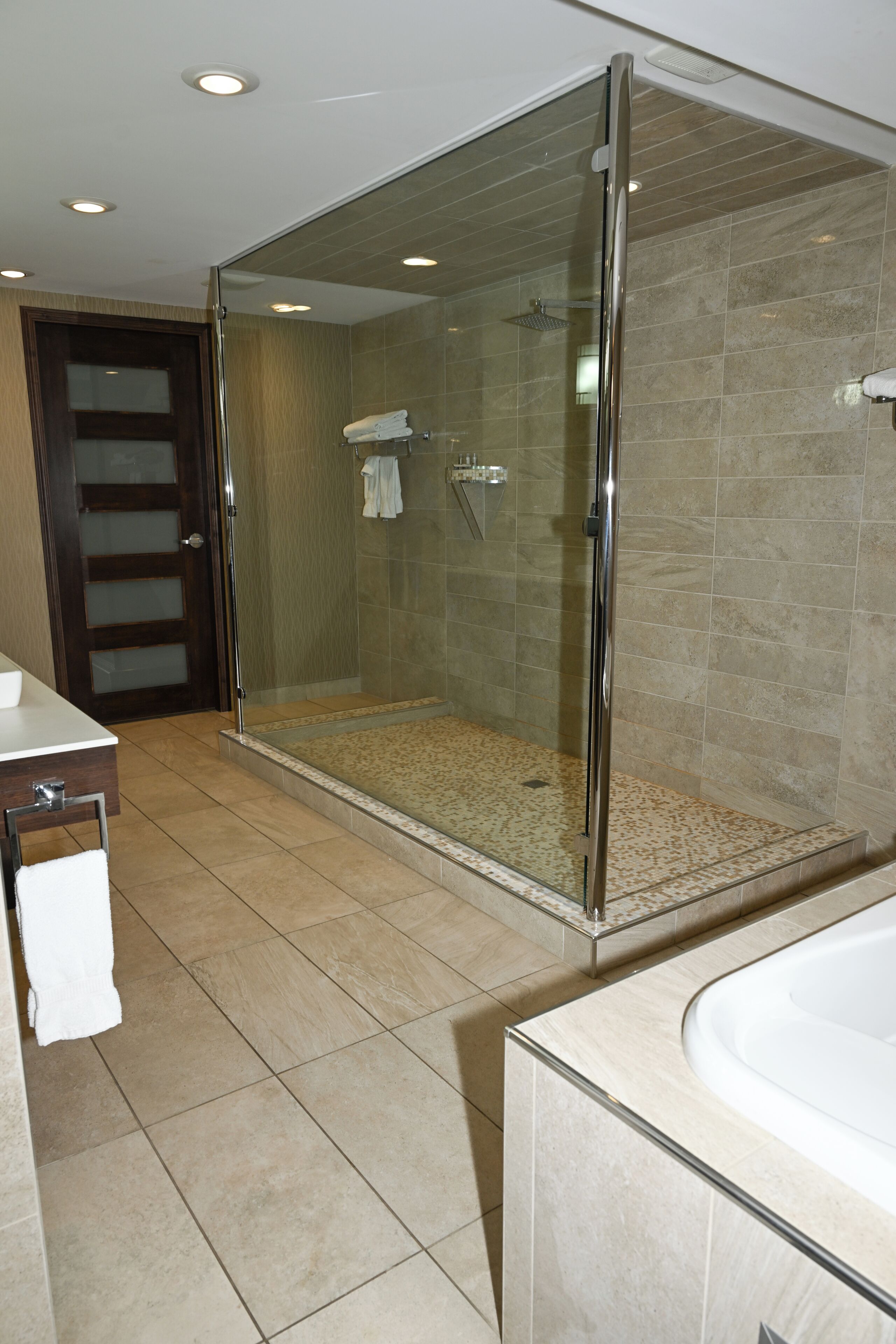 A modern bathroom with a glass-enclosed shower, a bathtub, and a vanity with a mirror.