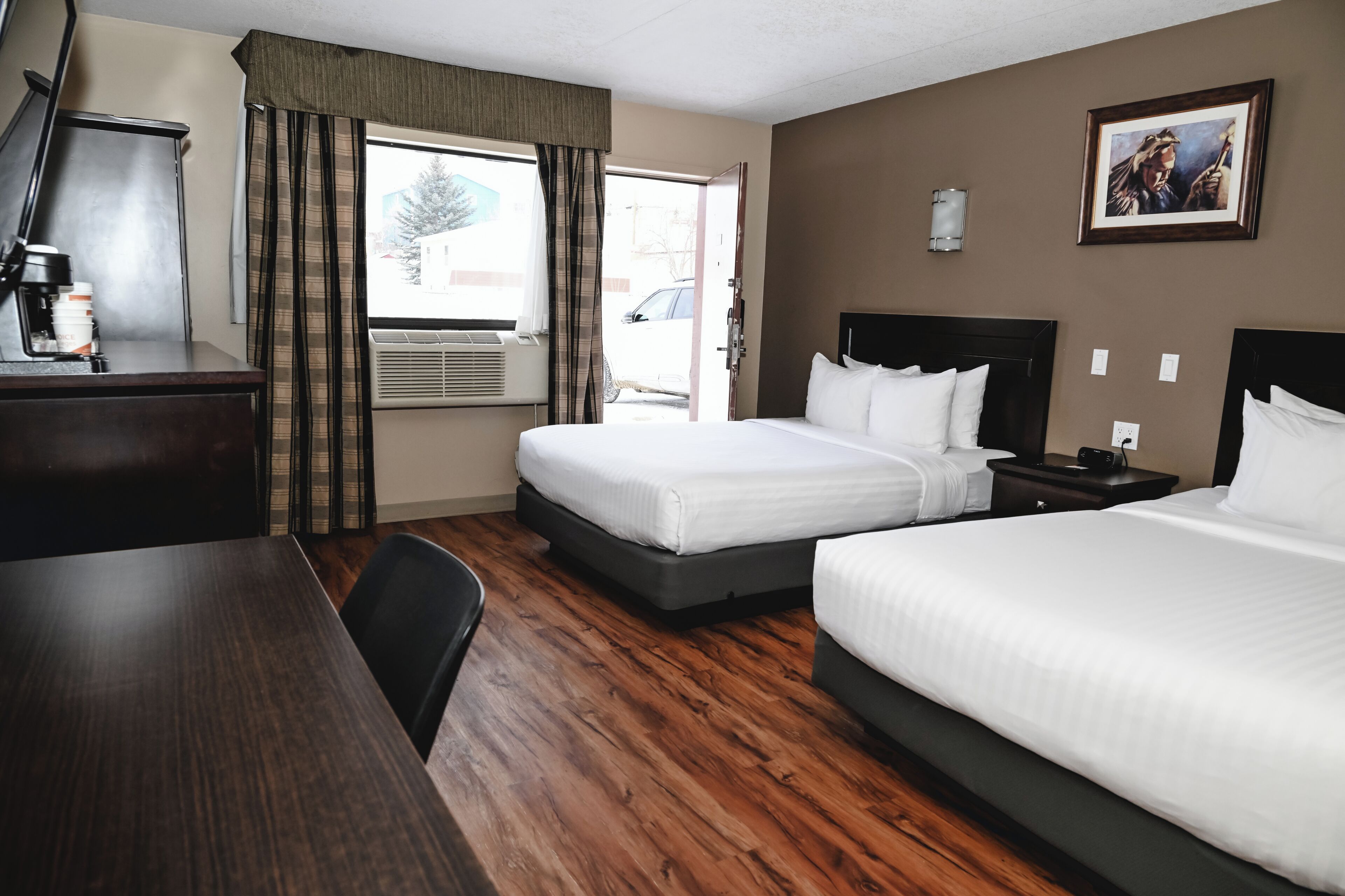 A hotel room with two beds, a desk, a chair, and a window with curtains.