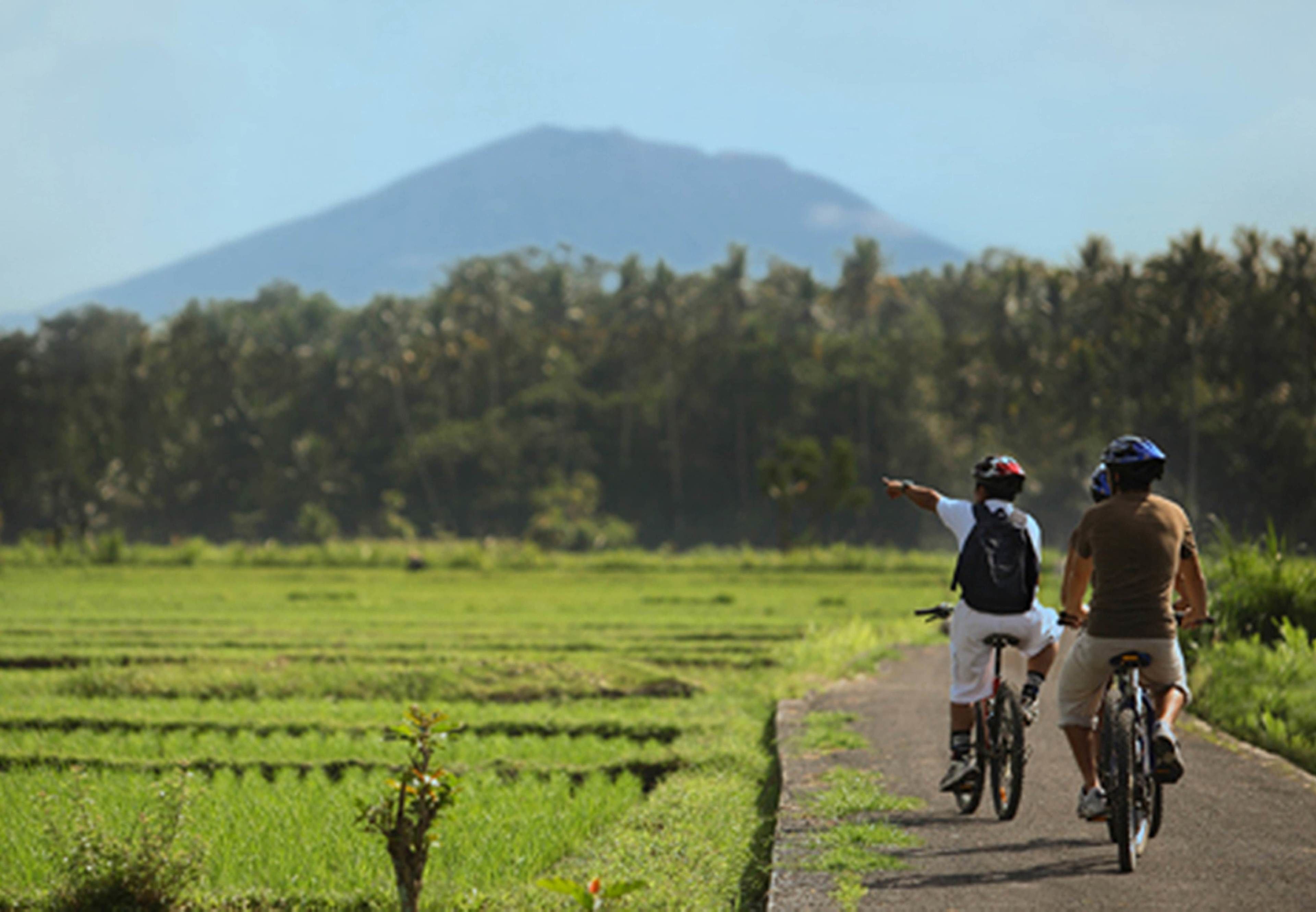 Two cyclists on a paved path with a mountain in the background.