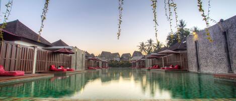 A pool area with tiled flooring, lounge chairs, and umbrellas.