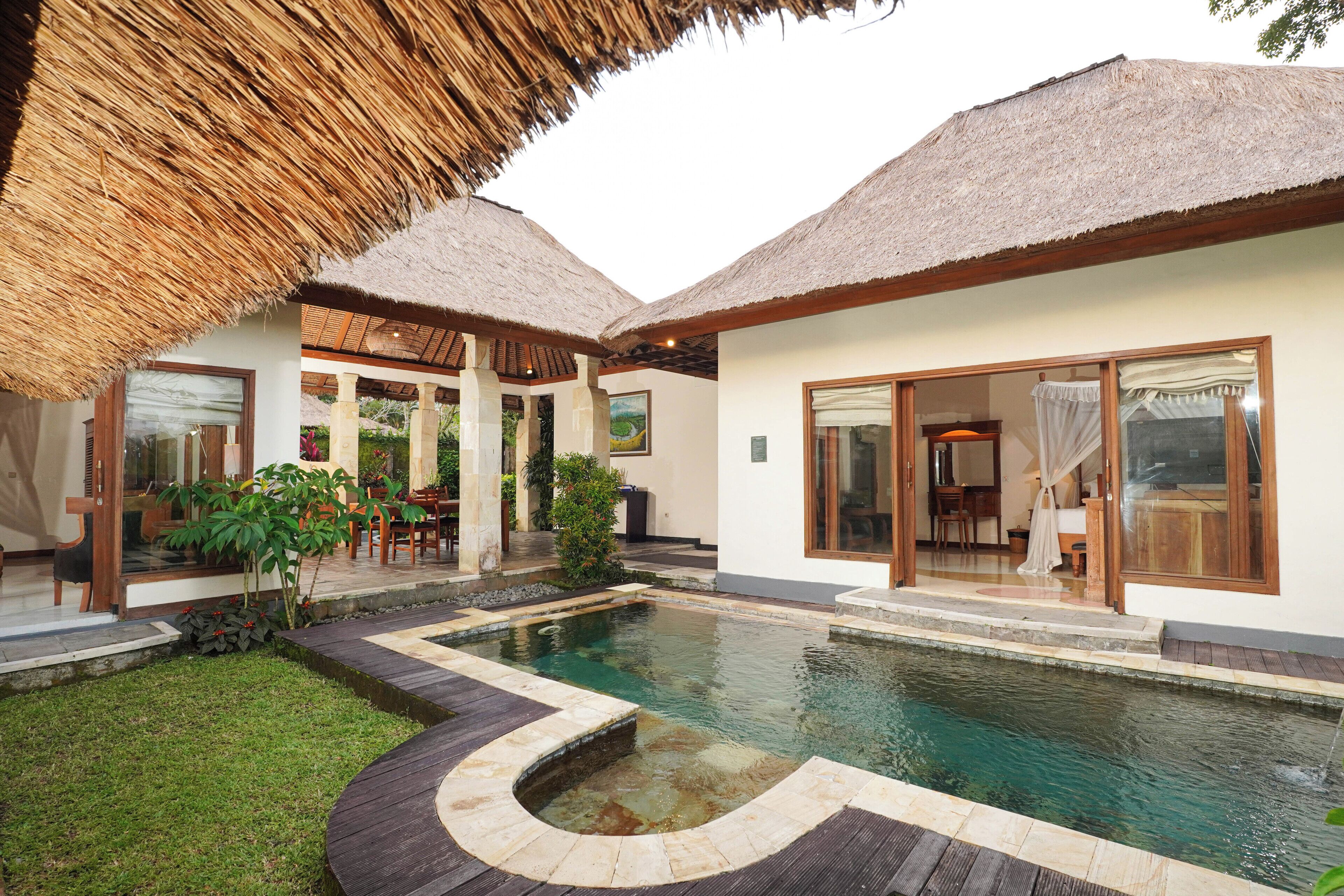Un área de piscina con una estructura de techo de paja, césped bien cuidado y un comedor con mobiliario exterior.
