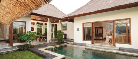 Un área de piscina con una estructura de techo de paja, césped bien cuidado y un comedor con mobiliario exterior.