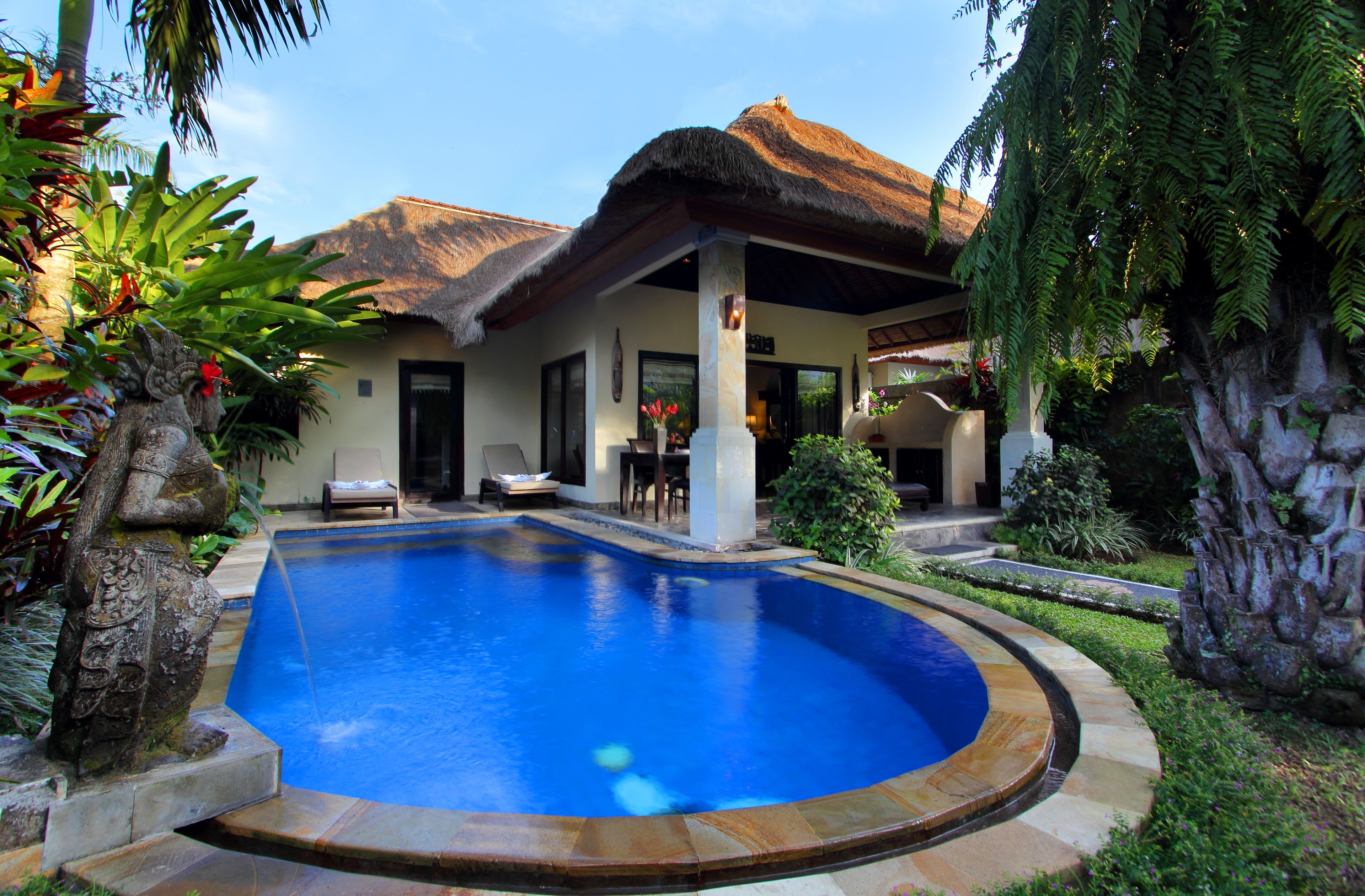 A swimming pool with a curved edge, a thatched-roof structure, and lush greenery.