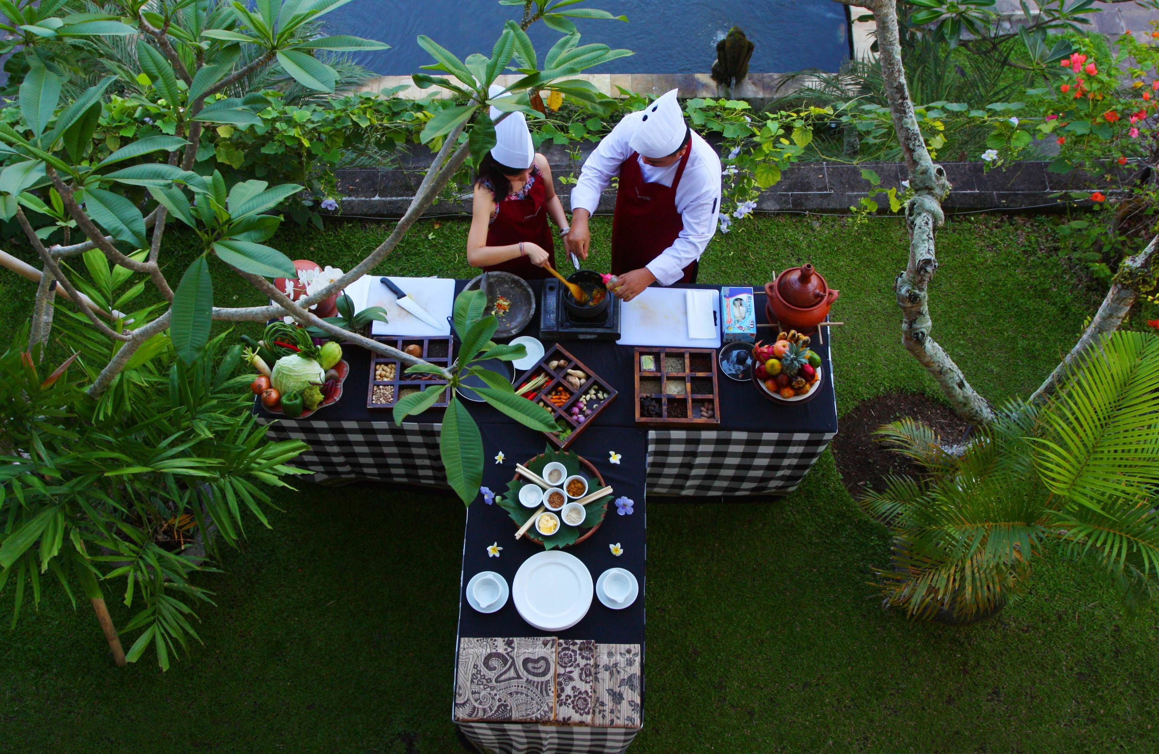 An outdoor dining setup with a checkered tablecloth, a variety of dishes, and a tropical garden background.