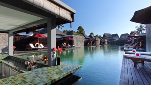 A resort pool area with lounge chairs, umbrellas, and a tiled deck. - FuramaXclusive Resort & Villas, Ubud (Mas)