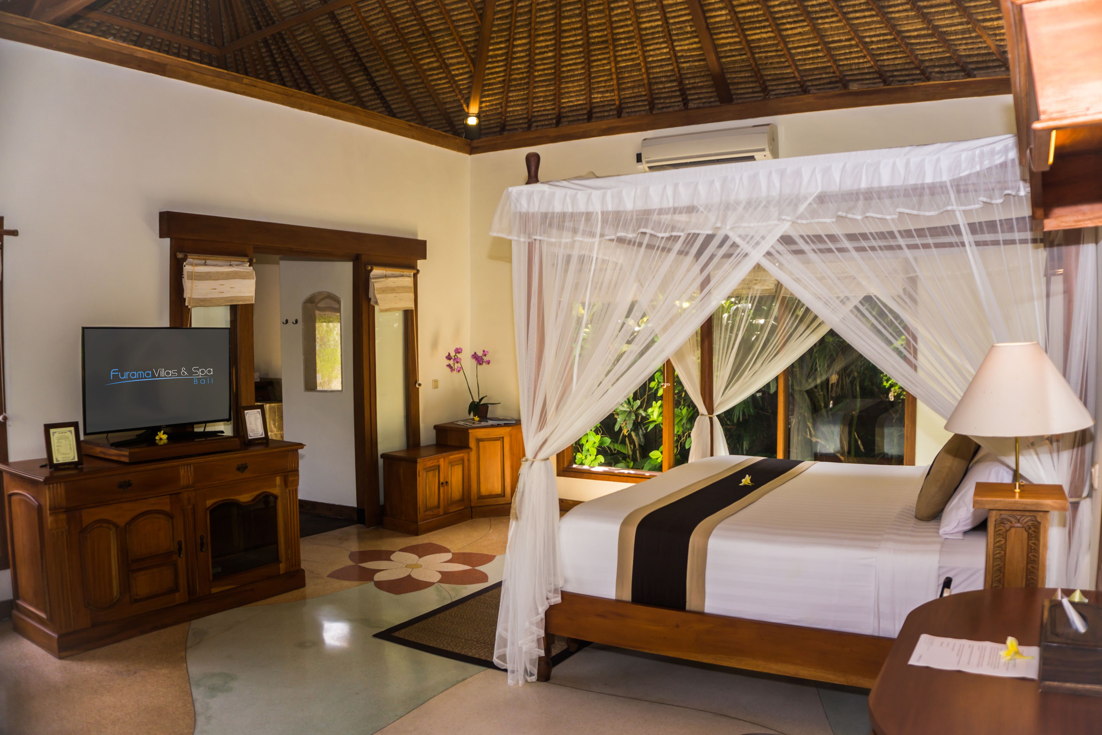A hotel room with a bed, a TV, a wooden cabinet, and a window with a view of greenery.