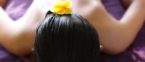 Une personne reçoit un massage du dos sur un lit dont la literie est de couleur violette.