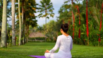 A person sitting on a purple mat in a grassy area with trees and red flags in the background.