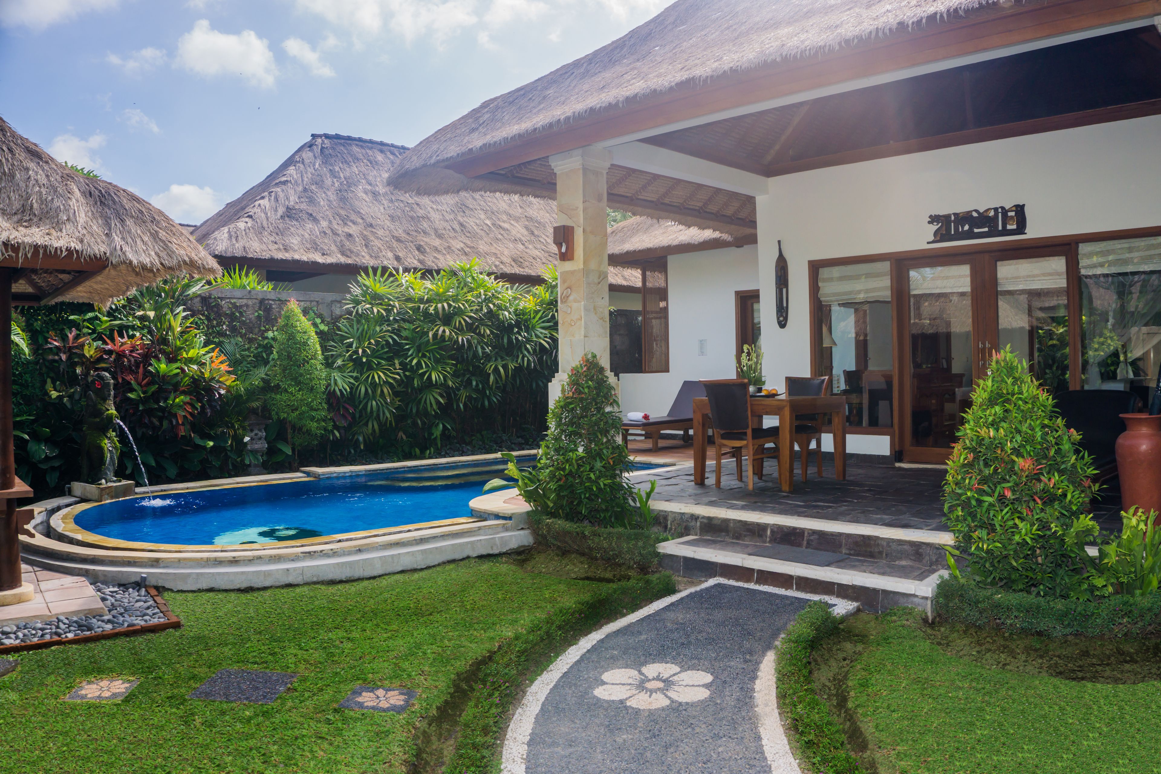 A pool with a thatched roof structure, a covered patio area with seating, and a well-maintained garden.