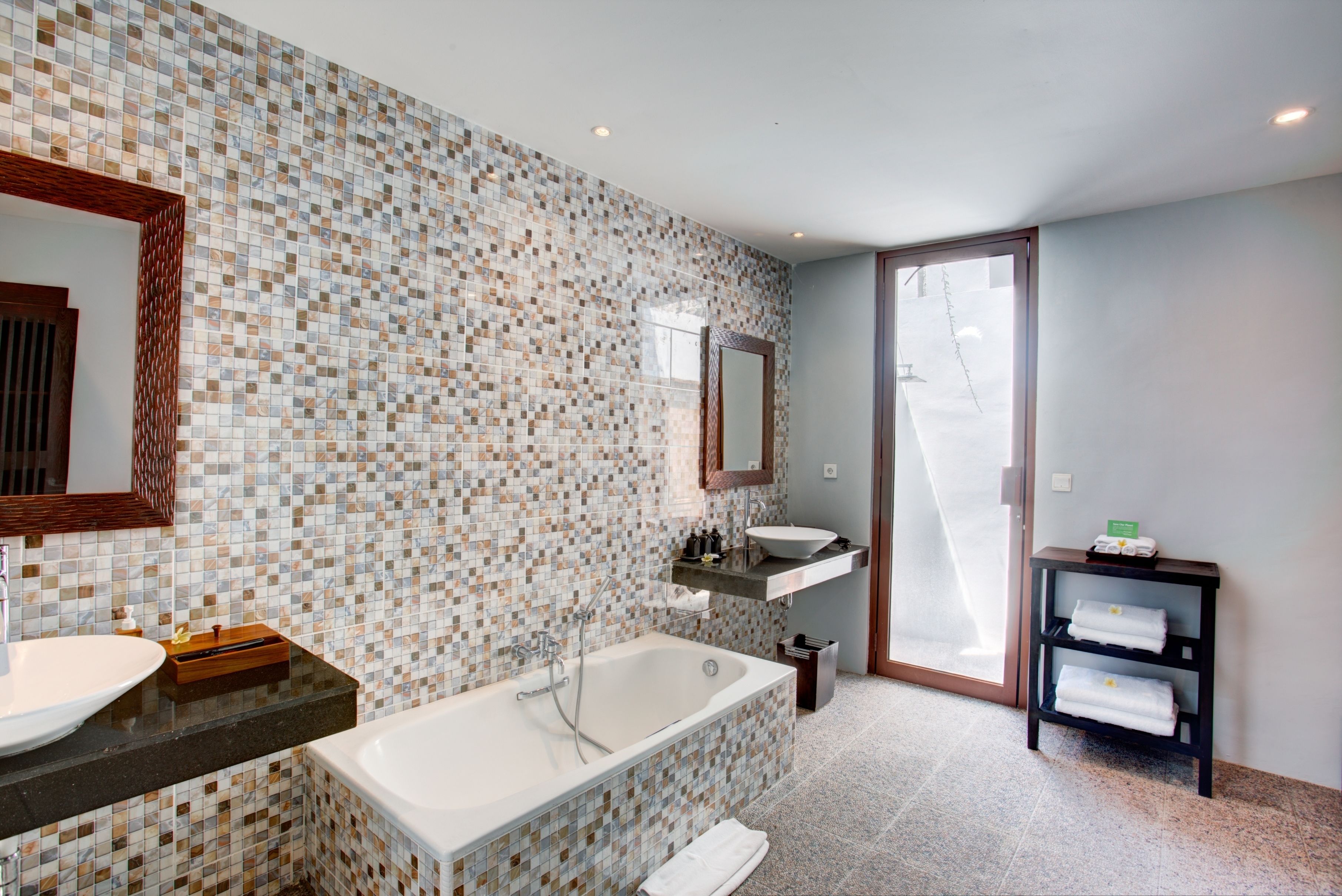 A modern bathroom with a mosaic tile backsplash, a freestanding bathtub, a vanity with a sink, and a mirror above the mirror.