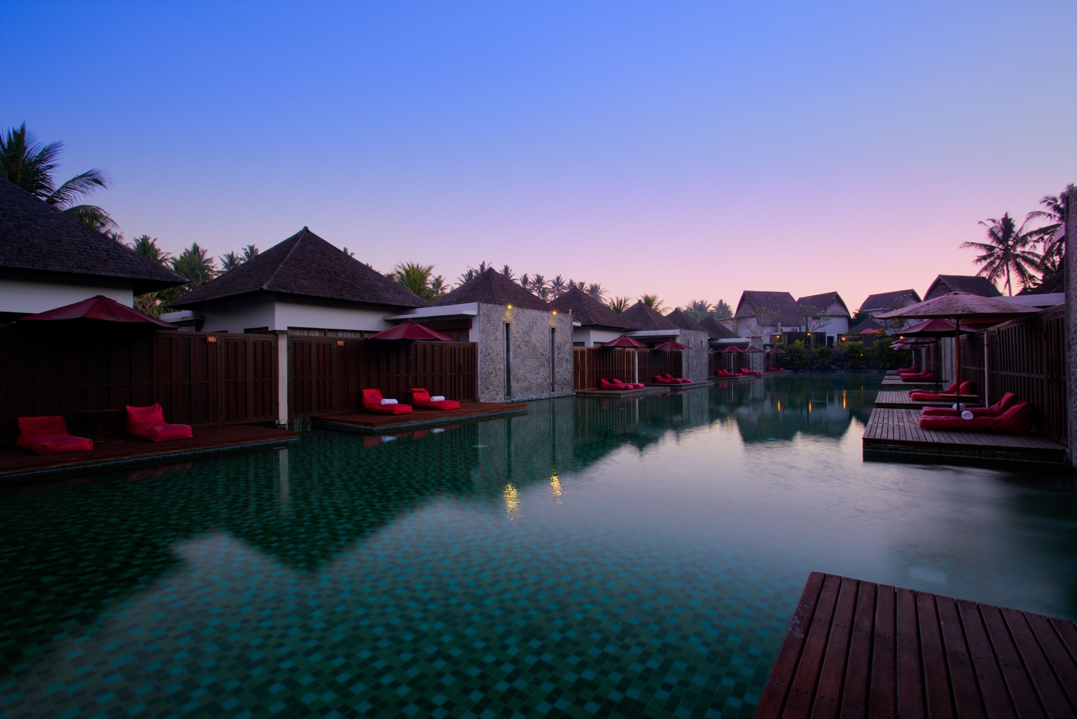 A serene pool area with overwater bungalows, each with a thatched roof and wooden deck.