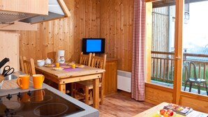 A wooden interior with a kitchen, dining area, and a view through a sliding door.
