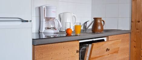 A kitchen with a coffee maker, a pitcher, a glass of orange juice, and wooden cabinets.