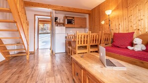 A wooden interior with a kitchen, a dining area, and a seating area with a laptop on a table.