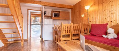 Un interior de madera con cocina, zona de comedor y área de estar con una computadora portátil sobre una mesa.