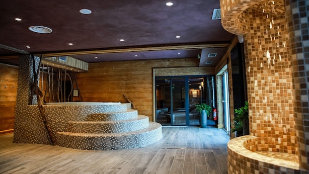 A modern interior with a wooden staircase, a tiled wall, and a glass entrance.
