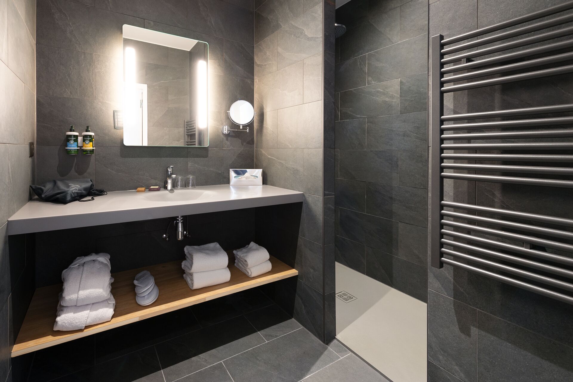 Un baño moderno con tocador, espejo, toallero y zona de ducha.