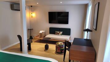 A compact hotel room with a bed, a desk, a chair, a sofa, a TV, and a lamp.