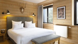 A wooden-paneled room with a large bed, two bedside lamps, a mounted deer skull, a framed picture, and a window with curtains.