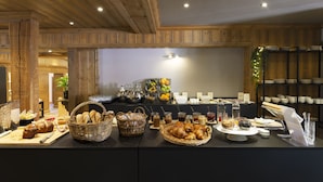 A breakfast buffet with various breads, pastries, and beverages.