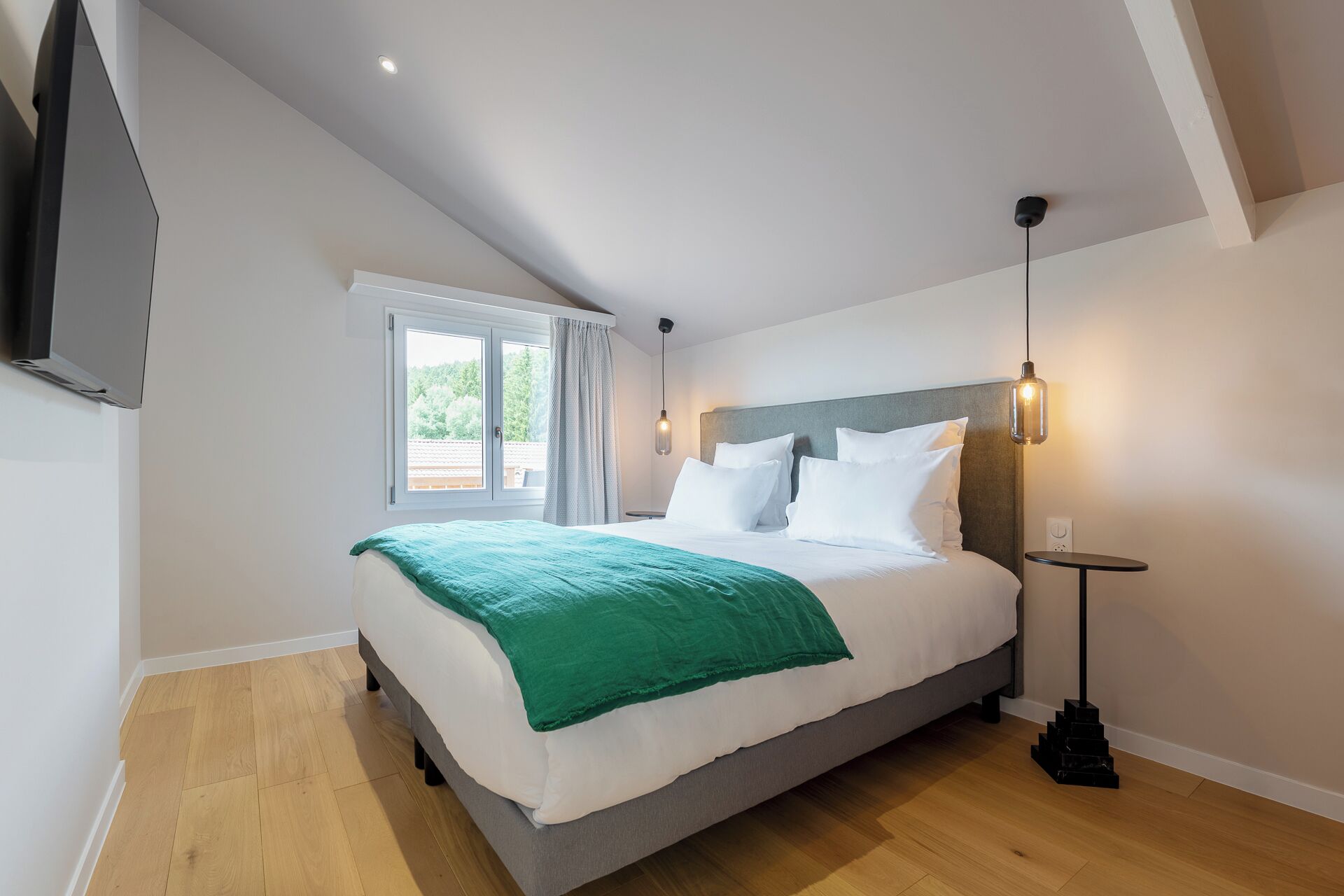 Una habitación de hotel moderna con una cama grande, un televisor de pantalla plana, una ventana con cortinas y una lámpara de techo original.