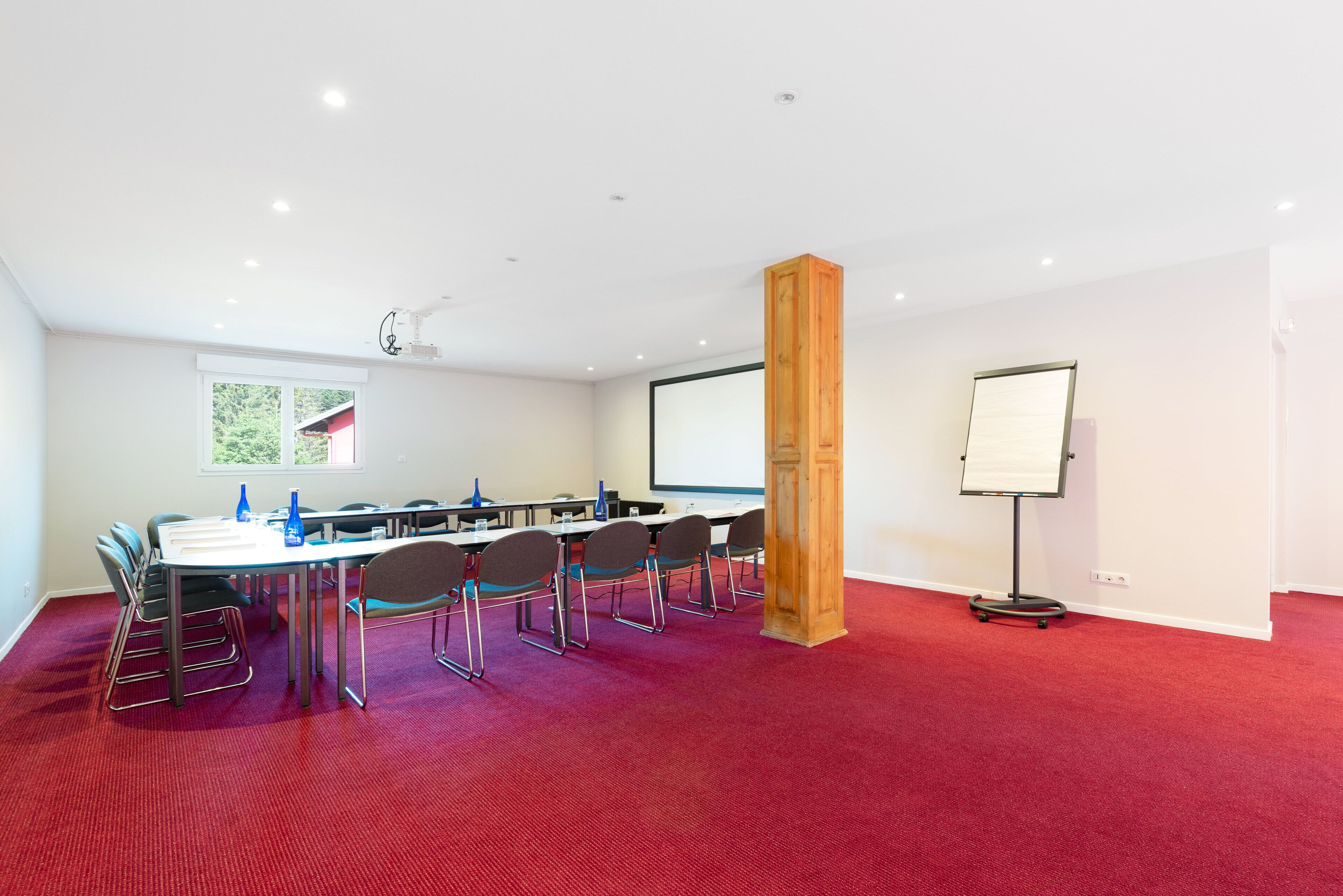 A conference room with a red carpet, a whiteboard, a projector screen, and a wooden pillar.