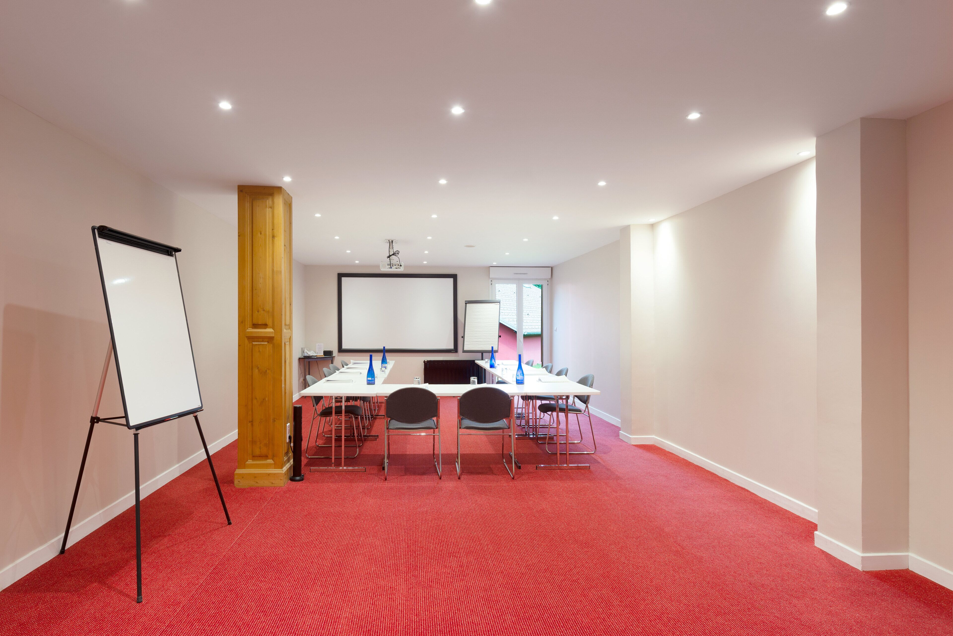 Une salle de conférence équipée d’un tableau blanc, d’un écran de projection et d’un sol recouvert d’une moquette rouge.
