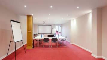 Une salle de conférence équipée d’un tableau blanc, d’un écran de projection et d’un sol recouvert d’une moquette rouge.