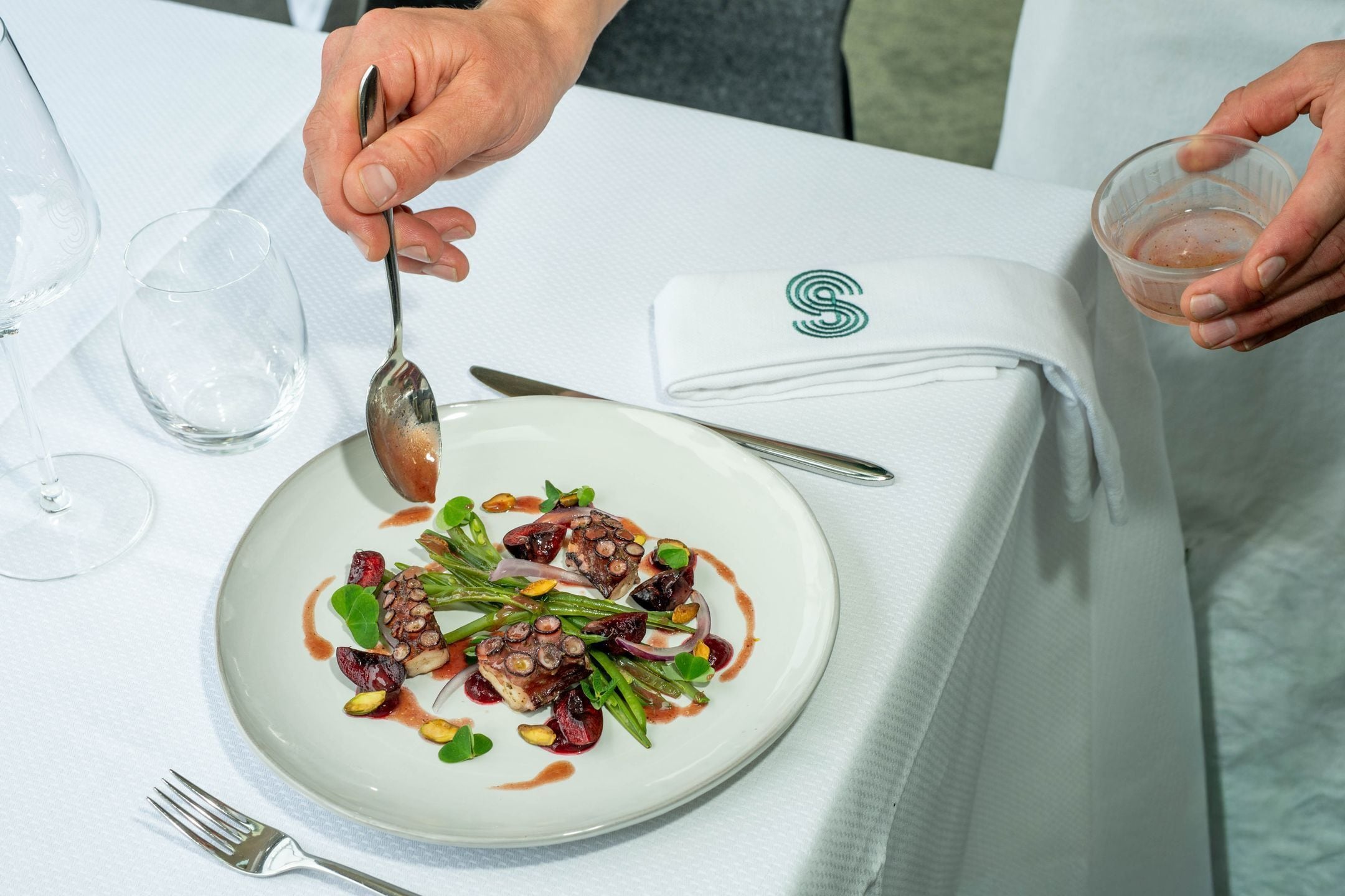 Una mesa de comedor con un plato de comida, una cuchara, un tenedor y un vaso de agua.