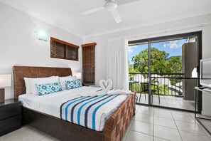 A modern hotel room with a large bed, a balcony with a view of trees, and a ceiling fan. - Blue Lagoon Resort (Trinity Beach)