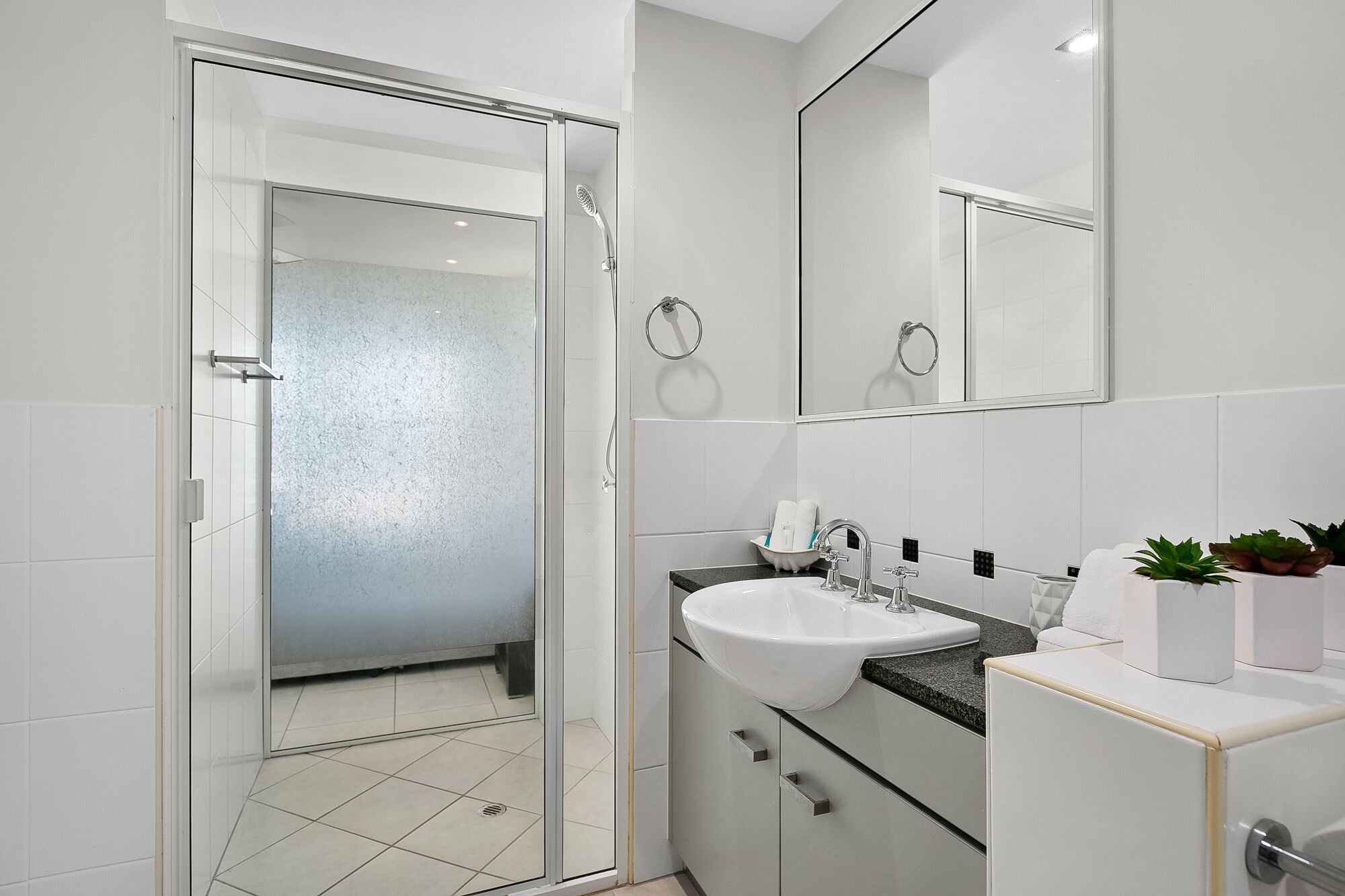 Un baño moderno con mampara de vidrio, un lavabo blanco y un espejo sobre el lavabo.