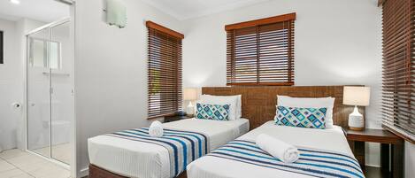 Habitación de hotel con dos camas, ventilador de techo y persianas de madera en las ventanas.