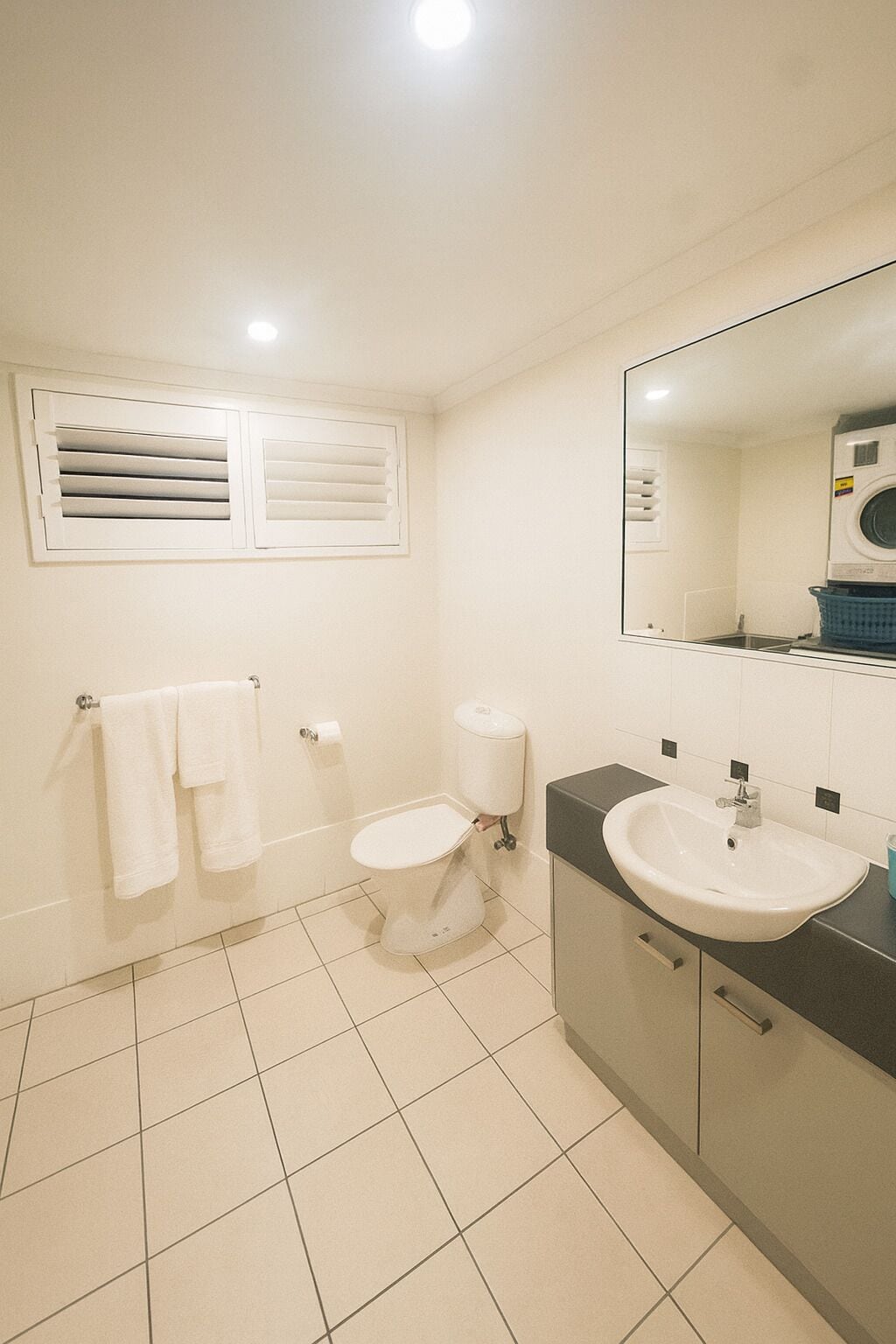 A bathroom with a toilet, sink, mirror, and a window with blinds.